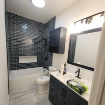 Completed bathroom remodel with grey stone shower, pebble floor, and white vanity